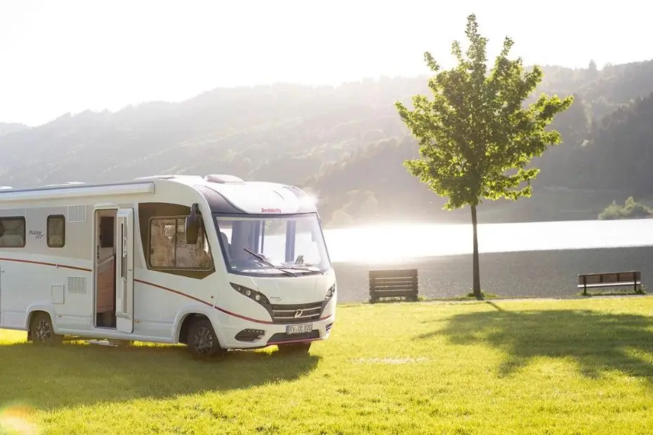 Wohnmobil mit offener Tür auf einen Rasen am Seeufer zum Thema Reisetipps: Camping und Angeln